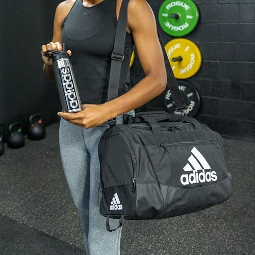 Person holding Adidas gym bag and bottle in fitness setting.