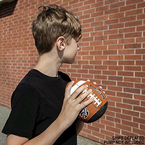 Boy holding a football near a brick wall.