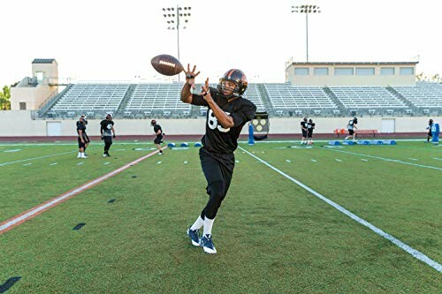 Football player catching a ball on a field with teammates in the background.