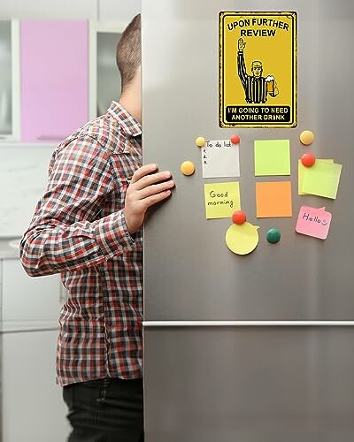 Person partly hidden by a fridge with notes and a humorous magnet.